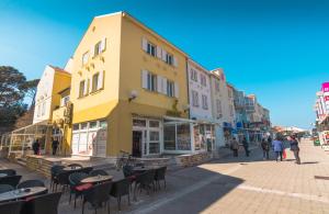 a yellow building on a street with tables and chairs at Apartment Vita in Rab