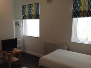 a bedroom with a bed and two windows and a television at Repton Private Hotel in Romford