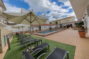 eine Terrasse mit Stühlen, einem Sonnenschirm und einem Pool in der Unterkunft Hotel Apartamentos Loto Conil in Conil de la Frontera