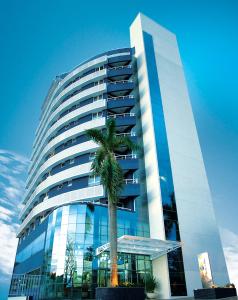 a tall building with a palm tree in front of it at Golden Blue Hotel in Londrina