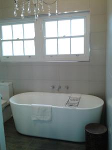 a white bath tub in a bathroom with two windows at Casa Rossa - Barossa in Lyndoch
