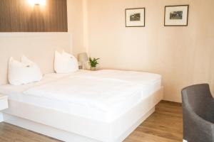 ein weißes Bett in einem Zimmer mit Stuhl in der Unterkunft Weddeler Hof in Cremlingen