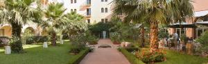 a courtyard with palm trees and a building at Alhambra Thalasso in Hammamet