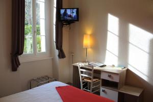 a bedroom with a bed and a desk and a television at Hotel des Thermes in Lamalou-les-Bains