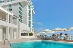 einen Pool neben einem Gebäude mit Tischen und Sonnenschirmen in der Unterkunft Oleo Cancun Playa All Inclusive Resort in Cancún