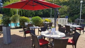 d'une terrasse avec des tables, des chaises et un parasol rouge. dans l'établissement Mercure Paris Le Bourget Aeroport, au Blanc-Mesnil