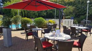 a patio with tables and chairs with a red umbrella at Mercure Paris Le Bourget Aeroport in Le Blanc-Mesnil