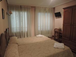 a bedroom with two beds and a dresser and curtains at Hostal Villa de Navarrete in Navarrete