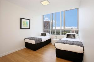 two beds in a room with a large window at Moore to See - Modern and Spacious 3BR Zetland Apartment with Views over Moore Park in Sydney