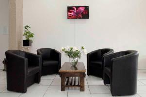 una sala de espera con 3 sillas y una mesa con flores en Hotel Igrejinha, en Igrejinha