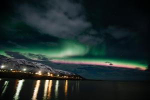 an aurora in the sky over the water at night at Blabjorg Resort in Borgarfjordur Eystri