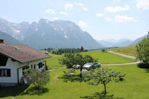 a house with a car parked in a field with mountains at Zum Bergbauer in Mittenwald