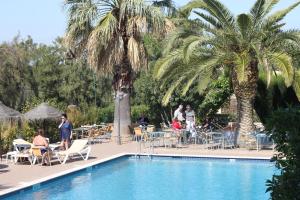 una piscina con palmeras y gente sentada a su alrededor en Hotel Pinhal do Sol, en Quarteira
