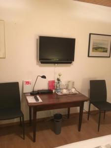 einen Schreibtisch mit einem TV an der Wand mit 2 Stühlen in der Unterkunft Bed & Breakfast aux Enges in Enges