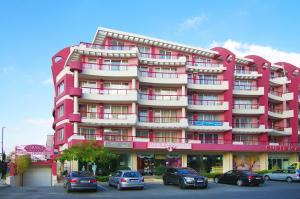 un edificio rosa con coches estacionados frente a él en Cabana Beach Club Complex, en Nesebar