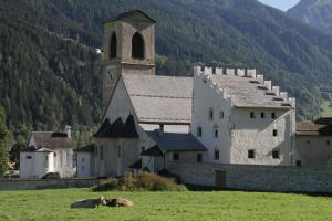Eine Kuh liegt auf einer Wiese vor einer Kirche in der Unterkunft Hotel Chavalatsch in Taufers im Münstertal