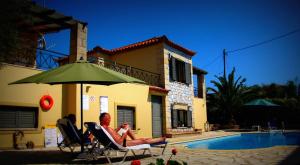 a man sitting in chairs under an umbrella next to a pool at Finikes Apartments in Stoupa