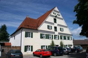 Una gran casa blanca con ventanas verdes y coches aparcados en Gasthof Adler en Zusmarshausen