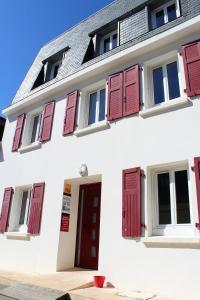 a white building with red shuttered windows and a red door at Gite de la Baie - Morgat in Crozon