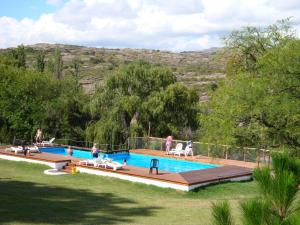 a swimming pool with people sitting on chairs in the grass at Cabañas El Refugio de Juan in Mina Clavero