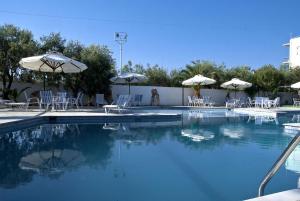 a swimming pool with tables and chairs and umbrellas at Klonos Anna in Egina
