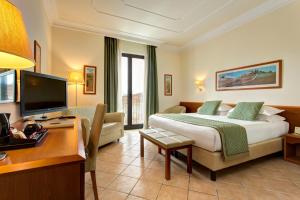 um quarto de hotel com uma cama, uma secretária e uma televisão em Hotel Athena em Siena