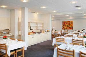 um restaurante com mesas e cadeiras brancas e uma cozinha em Herning City Hotel em Herning