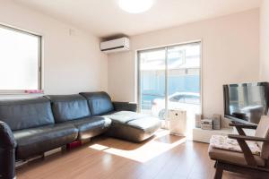 a living room with a black leather couch and a tv at Hinode House in Funabashi