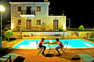 two boys sitting at a table next to a pool at Villas Panorama Apolpaina Lefkas in Apolpaina