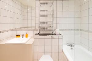 a white tiled bathroom with a sink and a tub at The California - London Kings Cross in London +37 photos