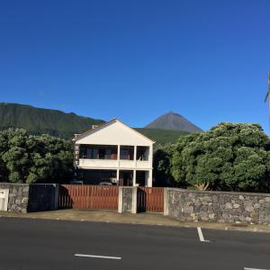 a white house with a fence and mountains in the background at Adega do Pereirinha in São Roque do Pico