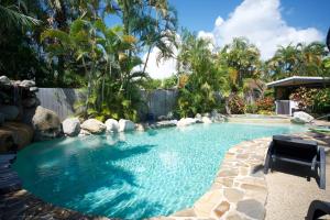 einen Pool in einem Garten mit Palmen in der Unterkunft Lazy Lizard Motor Inn in Port Douglas