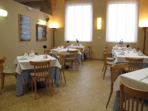 un comedor con mesas y sillas blancas y ventanas en Hotel Villa de Ayerbe, en Ayerbe