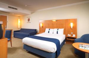 une chambre d'hôtel avec un lit et deux chaises bleues dans l'établissement Holiday Inn London - Heathrow M4,Jct.4, an IHG Hotel, à Hillingdon