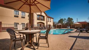 a table with chairs and an umbrella next to a pool at Best Western Bayou Inn and Suites in Lake Charles