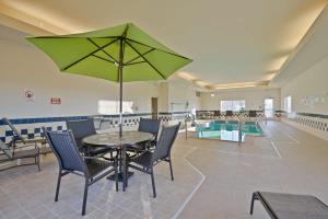 einen Tisch und Stühle mit einem grünen Sonnenschirm im Pool in der Unterkunft SureStay Hotel by Best Western Blackwell in Blackwell