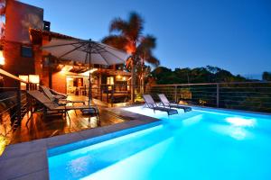 a swimming pool with chairs and an umbrella next to a house at Villa Gardena Suites in Praia do Rosa
