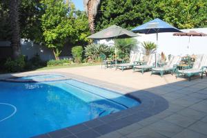 a swimming pool with chairs and umbrellas and a table and chairs at 6 on Morris Guest Lodge in Johannesburg