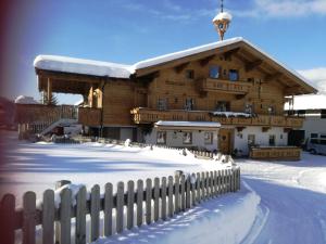 ein großes Holzgebäude mit einem Zaun im Schnee in der Unterkunft Bodenhof Ferienwohnungen in Fieberbrunn