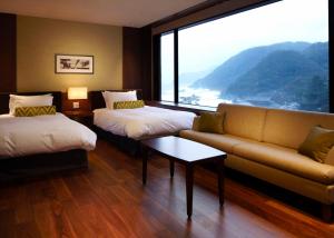 a room with two beds and a couch and a large window at Hotel Kinparo in Toyooka