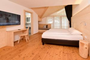 a bedroom with a bed and a desk and a television at Hotel Silvana in Selva di Val Gardena