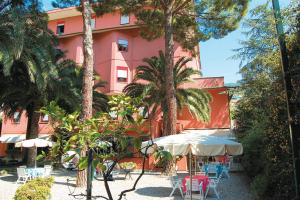 un edificio rosa con mesas, sillas y palmeras en Hotel Palme, en Monterosso al Mare