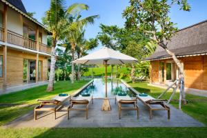un patio al aire libre con sillas y una sombrilla junto a la piscina en Alea Estate, en Kerobokan