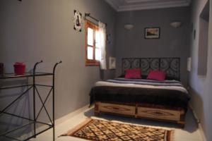 Un dormitorio con una cama con almohadas rosas y una ventana en Maison d'hôtes Dar El Nath, en Ouarzazate