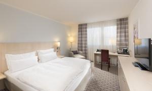 a hotel room with a large white bed and a desk at Mercure Hotel Mannheim am Friedensplatz in Mannheim