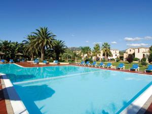 a large swimming pool with blue chairs and palm trees at Spacious Holiday Home in Sardinia with Swimming Pool in Pula