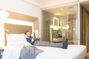 a man laying on a bed reading a book at Novotel RJ Porto Atlantico in Rio de Janeiro