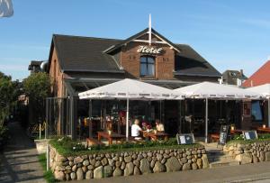 un restaurante con mesas y sombrillas frente a un edificio en Hotel Kiose - Ferienwohnungen en Wenningstedt