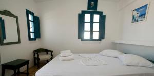 a bedroom with a white bed with a chair and windows at Oias Sunset in Oia