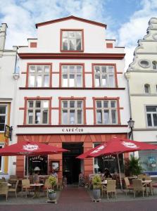 un bâtiment avec des tables et des parasols devant lui dans l'établissement Cafe 28 & Pension am Markt, à Wismar
